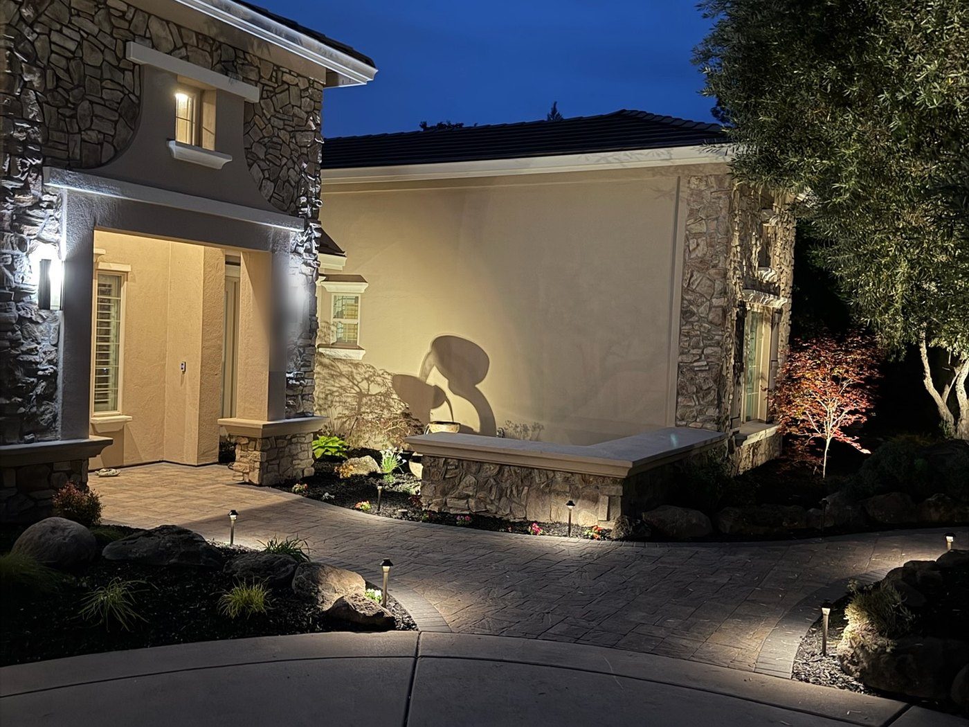 A stone-faced entry at dusk, uplit, with a low seat wall and planting either side of the door.